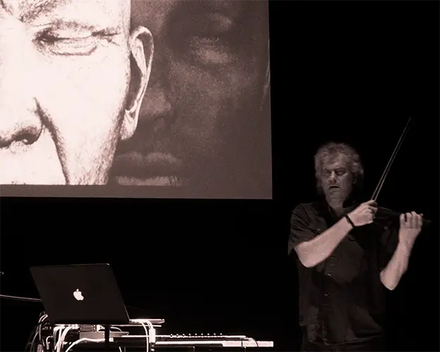 Mark Zaki performing violin and electronics beside a projected face