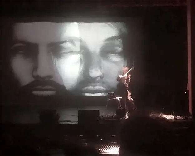 Mark Zaki performing before a large projected video portrait