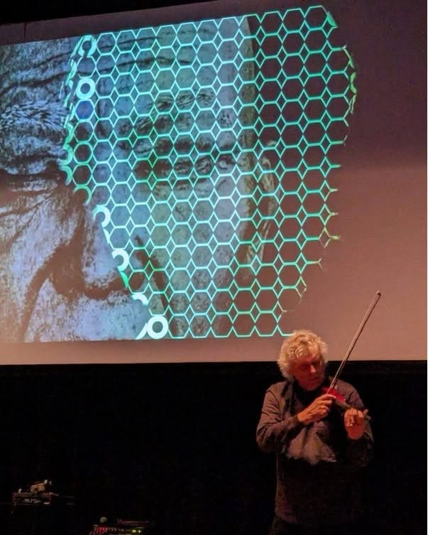 Mark Zaki performing violin beneath a geometric video projection