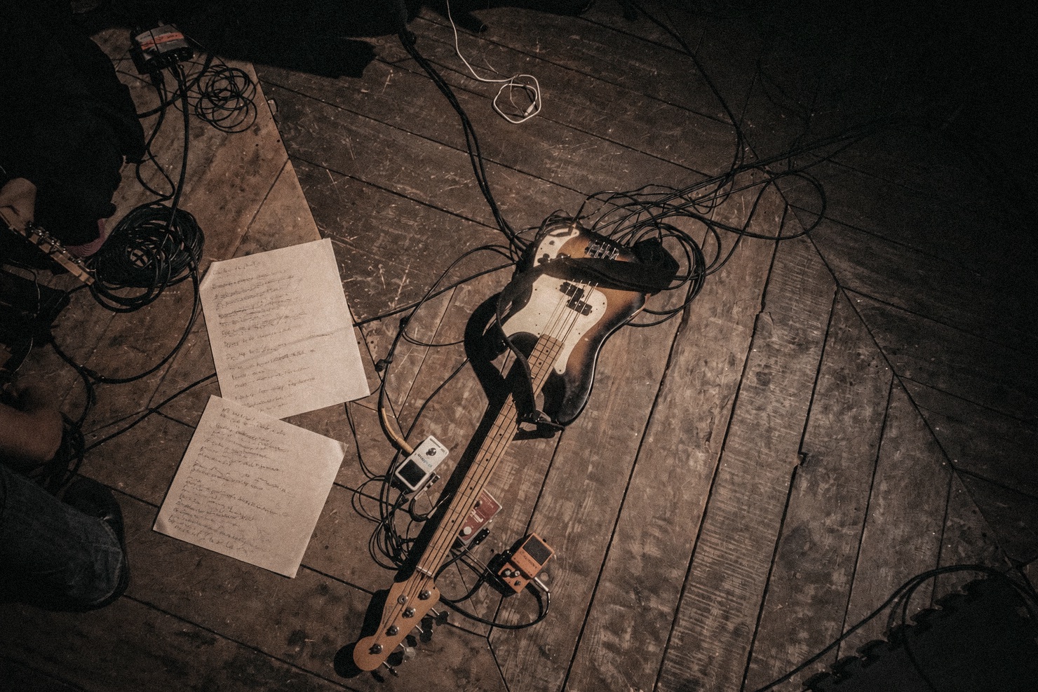 A bass guitar, cables, pedals, and handwritten music on a wooden stage